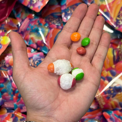 Skittles liofilizados de Frezzyks en una mano junto a su tamaño original